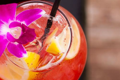 A refreshing cocktail with ice, lemon slices, and a purple orchid garnish.