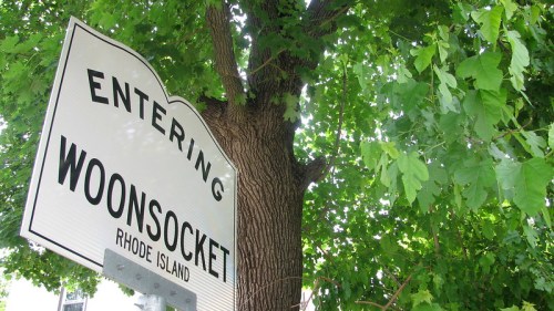 Sign reading "Entering Woonsocket, Rhode Island" with a large tree in the background.