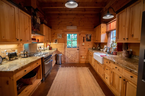 Cozy wooden kitchen with granite countertops, a farmhouse sink, and warm lighting, featuring rustic decor and a woven rug.
