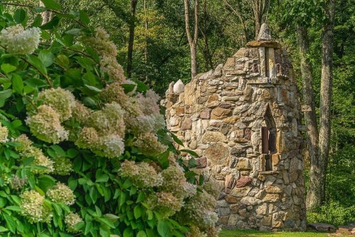 A stone ruin surrounded by lush greenery and blooming hydrangeas in a serene outdoor setting.