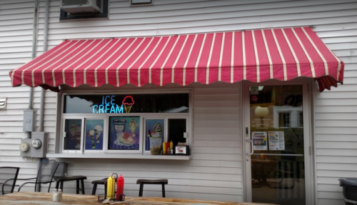 A quaint ice cream shop with a red and white striped awning, featuring a window display and outdoor seating.