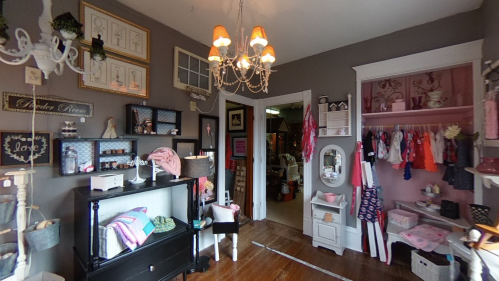A cozy boutique interior with shelves displaying clothing and accessories, a chandelier, and a pink-themed closet.