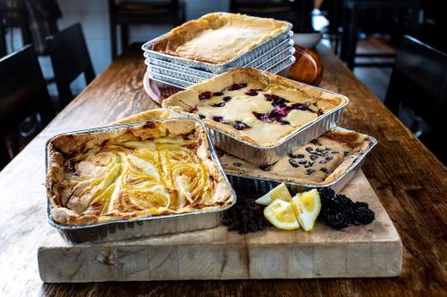 A wooden table displays several trays of baked desserts, including fruit tarts and a lemon slice, with blackberries scattered around.