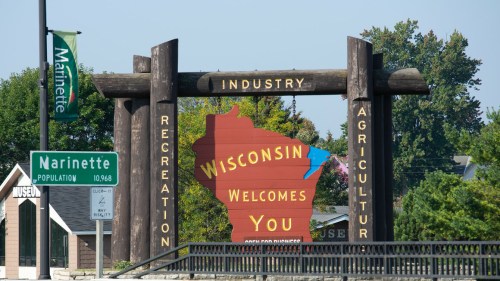 Sign welcoming visitors to Wisconsin, featuring the state outline and highlighting industry, recreation, and agriculture.