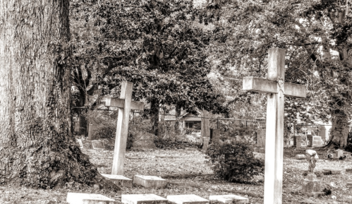 Black and white image of a cemetery with two crosses surrounded by trees and scattered gravestones.