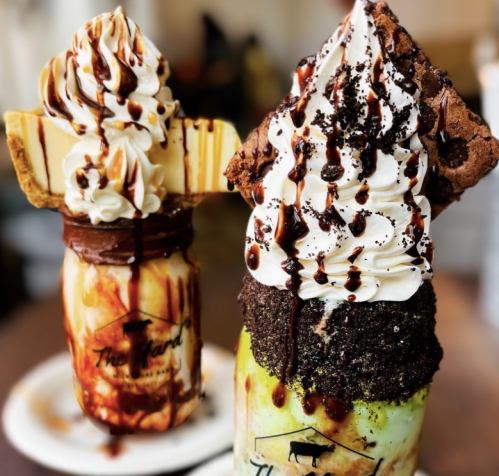 Two decadent milkshakes topped with whipped cream, chocolate drizzle, and cookie garnishes in mason jars.
