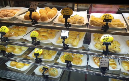 A display case filled with various baked goods, including buns and pastries, each labeled with prices.