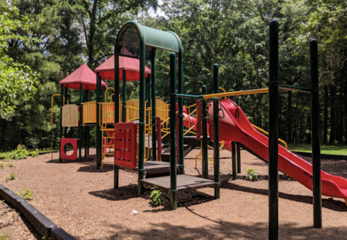 Colorful playground with slides and climbing structures, surrounded by trees and mulch.