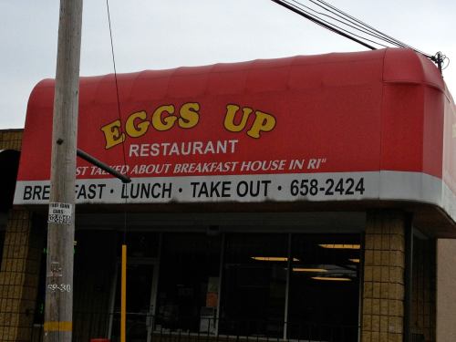 Red awning of "Eggs Up" restaurant, featuring signs for breakfast, lunch, and takeout in Rhode Island.