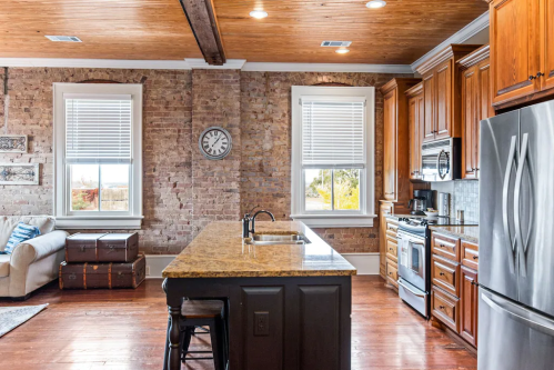 Modern kitchen with wooden cabinets, granite island, and exposed brick walls, featuring a cozy seating area.