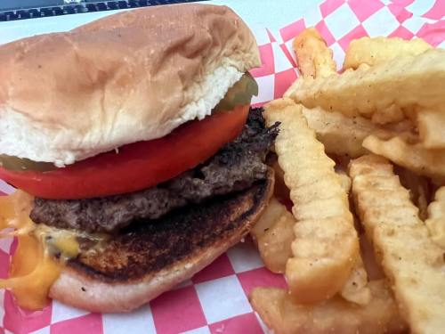 A close-up of a hamburger with lettuce, tomato, and pickles, served with crinkle-cut fries on a red-checkered paper.