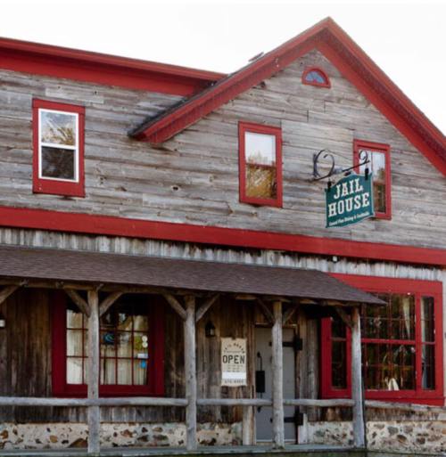 A rustic building with a wooden exterior, red accents, and a sign reading "Jail House" hanging above the entrance.