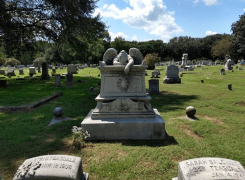 A large, ornate gravestone with two lion sculptures on top, surrounded by other gravestones in a grassy cemetery.