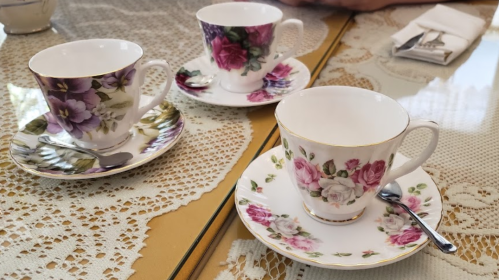 Three elegant teacups with floral designs on saucers, arranged on a lace tablecloth.