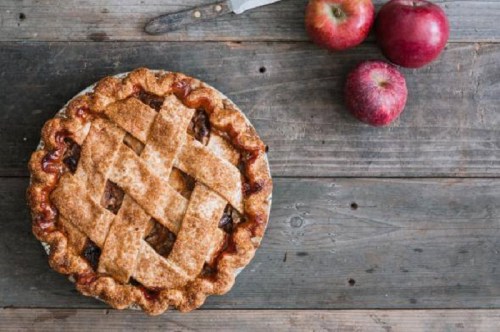 A freshly baked apple pie with a lattice crust, surrounded by red apples on a rustic wooden table.