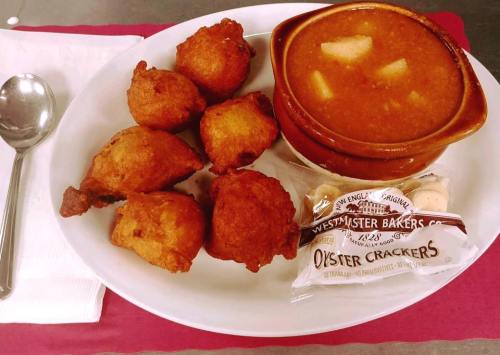 A plate with five golden fried fritters, a bowl of soup with potatoes, and a pack of oyster crackers on the side.