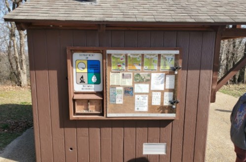 A wooden information kiosk with various signs and notices, set in a natural outdoor area.