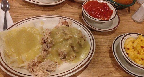A plate of shredded chicken with gravy over mashed potatoes, served with macaroni and cheese and a side of ketchup.