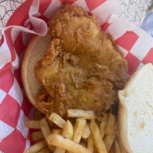 A crispy fried chicken sandwich on a bun, served with a side of golden French fries in a red and white checkered basket.