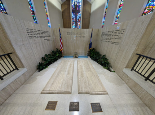 Interior view of a memorial with two stone slabs, flags, and stained glass windows, featuring engraved inscriptions.