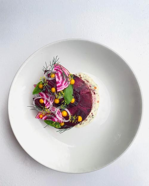 A beautifully plated dish featuring beets, colorful greens, and vibrant garnishes on a white plate.