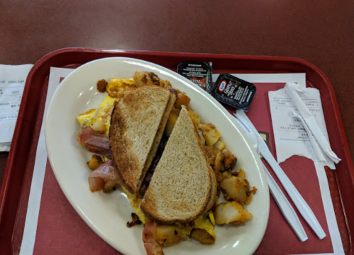 A plate with a sandwich, scrambled eggs, potatoes, and two packets of sauce on a red tray.