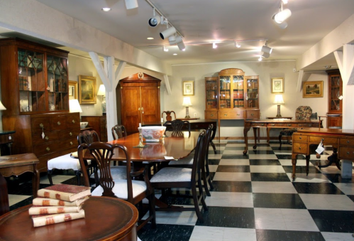 A well-furnished room with wooden furniture, a dining table, and a checkered floor, illuminated by overhead lights.