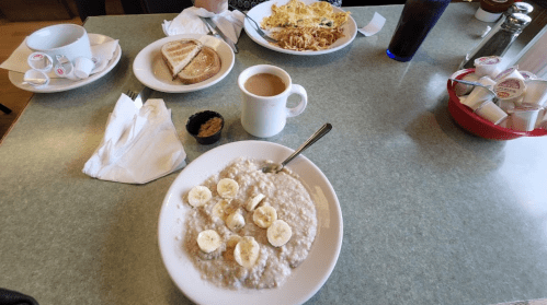 A table set with a bowl of oatmeal topped with banana slices, toast, an omelet, and a cup of coffee.