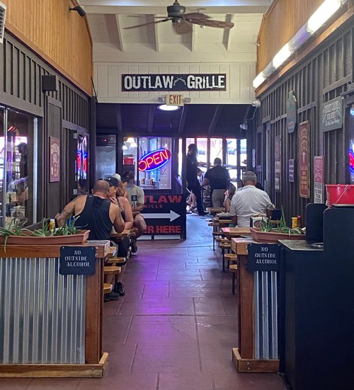 A narrow restaurant hallway with diners at tables, neon "OPEN" sign, and signs indicating no outside alcohol.