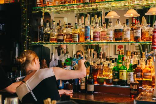 A bartender pours a drink at a well-stocked bar with various bottles of liquor displayed on shelves.