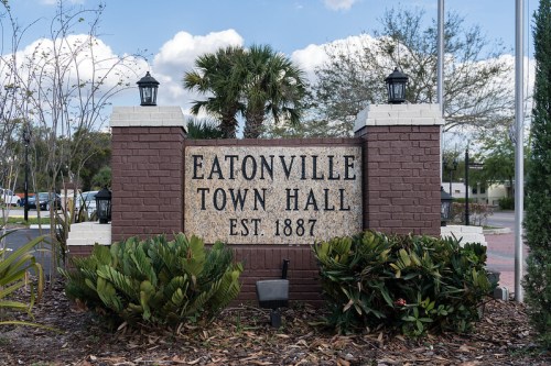 Sign for Eatonville Town Hall, established in 1887, surrounded by greenery and palm trees under a blue sky.