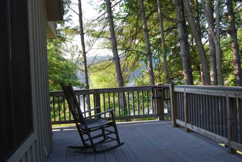 A wooden deck with a rocking chair, surrounded by tall trees and a view of a serene landscape in the background.