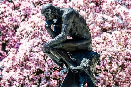 A bronze statue of a contemplative figure sits amidst blooming pink flowers.