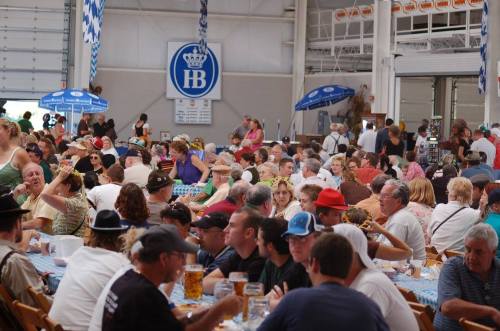 A large crowd of people enjoying a festive gathering in a spacious indoor venue, with tables and decorations.