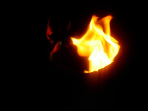 A bright flame flickers in a dark background, creating a warm and dynamic glow.