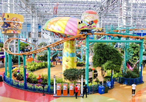 A colorful indoor amusement park with a roller coaster, vibrant decorations, and lush greenery.
