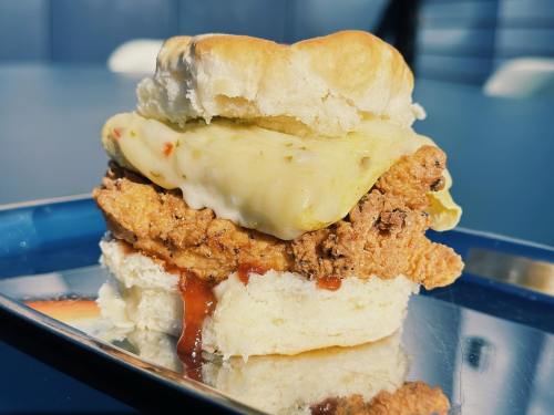 A close-up of a crispy chicken sandwich with melted cheese and sauce, served on a soft bun.