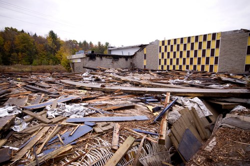 A devastated area with scattered debris and a partially collapsed building in the background.