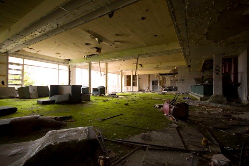 Abandoned interior of a building with overgrown moss, scattered debris, and deteriorating furniture.