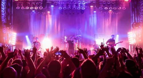 A lively concert scene with a band performing on stage, surrounded by an enthusiastic crowd with raised hands.