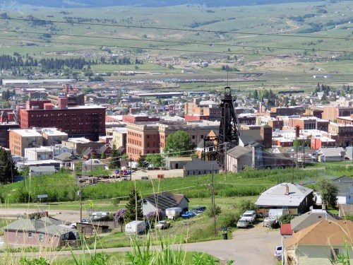 A panoramic view of a small town with buildings, a mining structure, and green hills in the background.