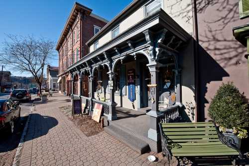 Historic buildings with ornate porches line a sunny street, featuring benches and decorative signs.