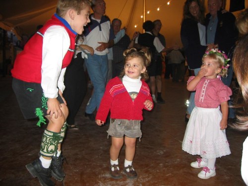 Children dancing joyfully at a festive event, with colorful outfits and a lively atmosphere in the background.