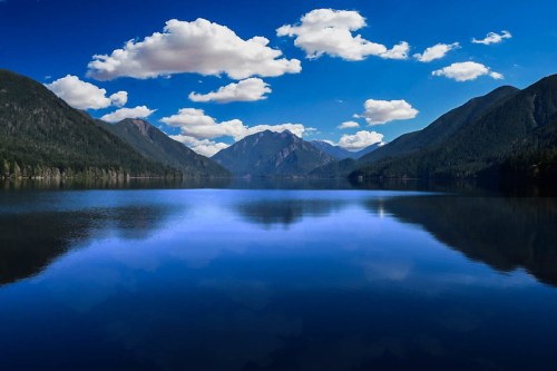 A serene lake surrounded by mountains, reflecting a clear blue sky with fluffy clouds.