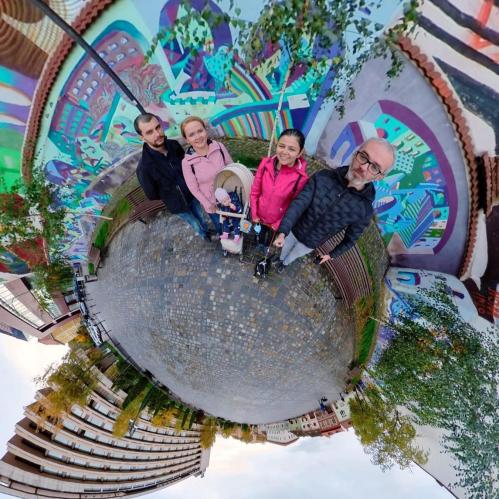 A family poses together in front of a colorful mural, with a stroller and vibrant surroundings.