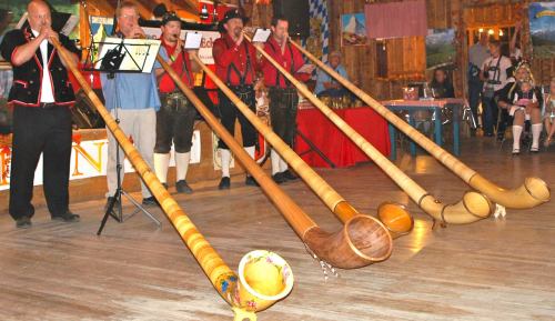 A group of musicians in traditional attire playing long wooden horns in a festive hall.
