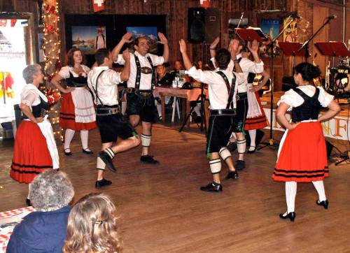 A group of dancers in traditional attire perform a lively dance in a festive setting with decorations and instruments.