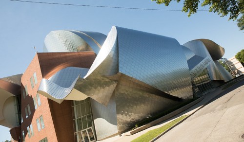 A modern building with a unique, wavy metallic facade and brick elements, set against a clear blue sky.