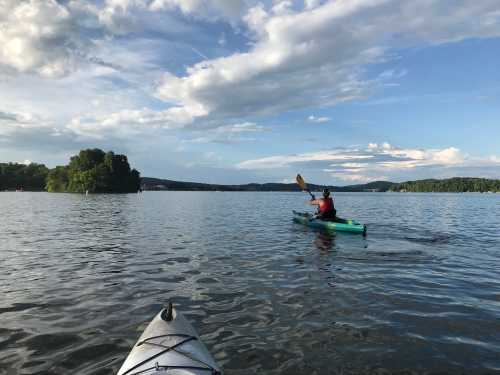 A person kayaking on a calm lake with a small island in the background and a scenic sky above.