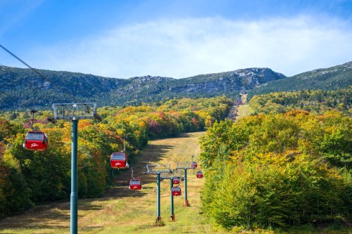 A scenic view of a ski lift with red gondolas, surrounded by colorful autumn foliage and mountains in the background.